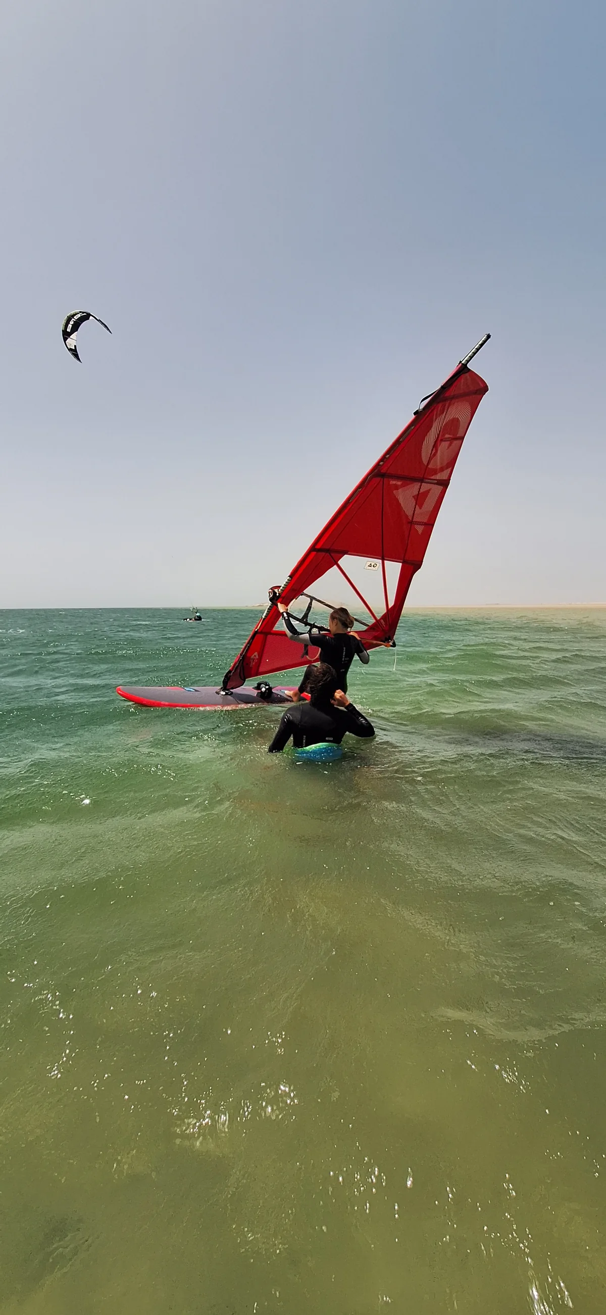 Windsurfer learning with a red sail in shallow water