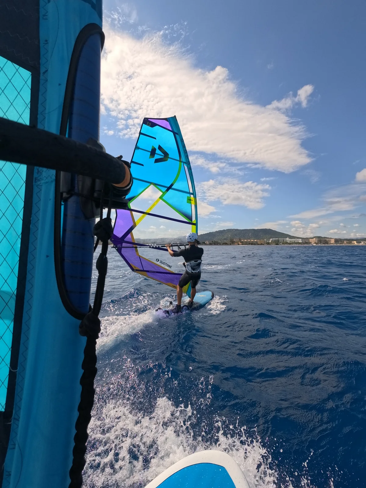 Close on-water coaching beside a blue and green sail